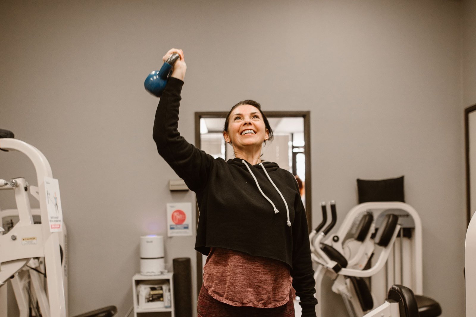 A woman pressing a kettlebell overhead in a gym