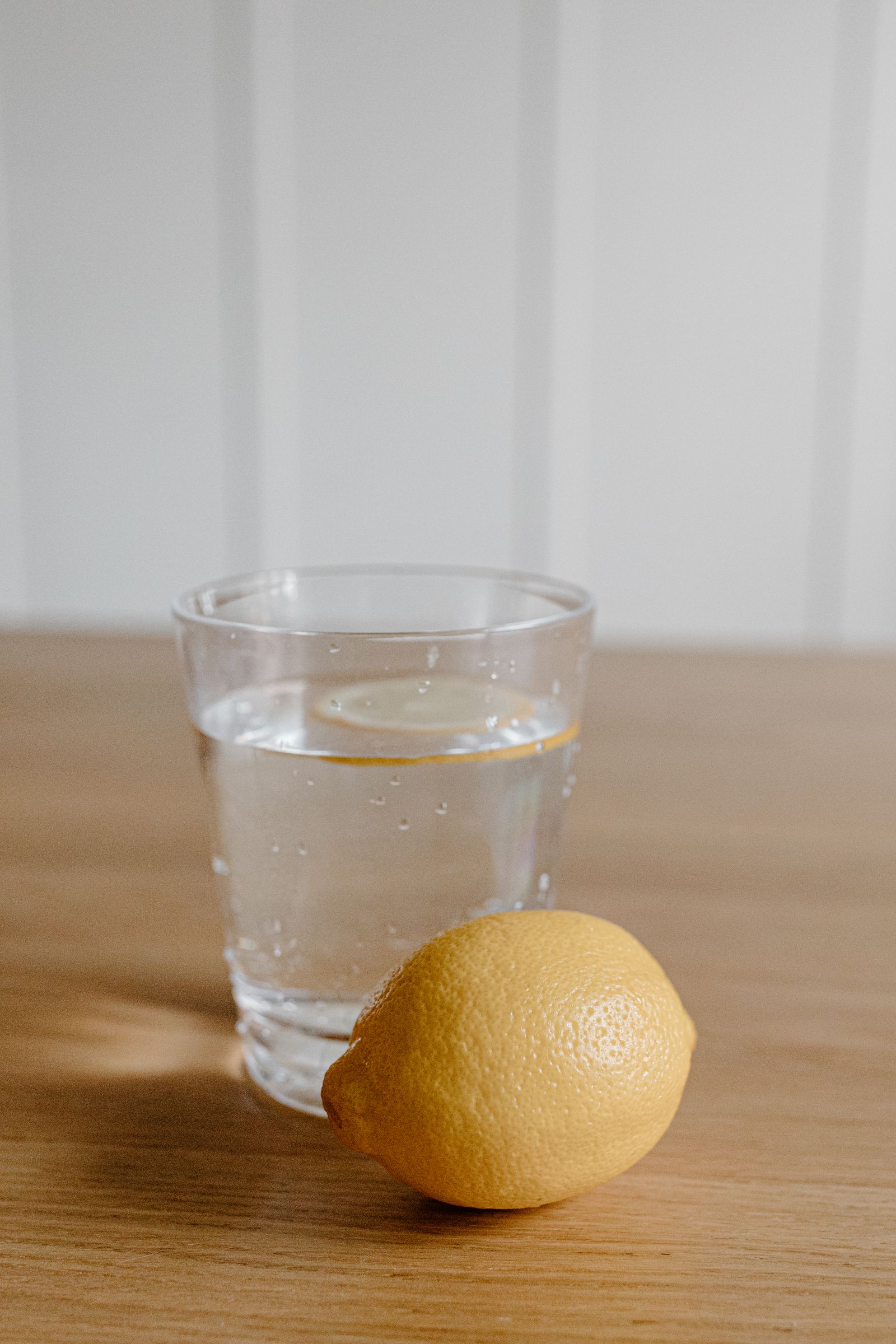 A glass of water with a lemon slice on a wooden table