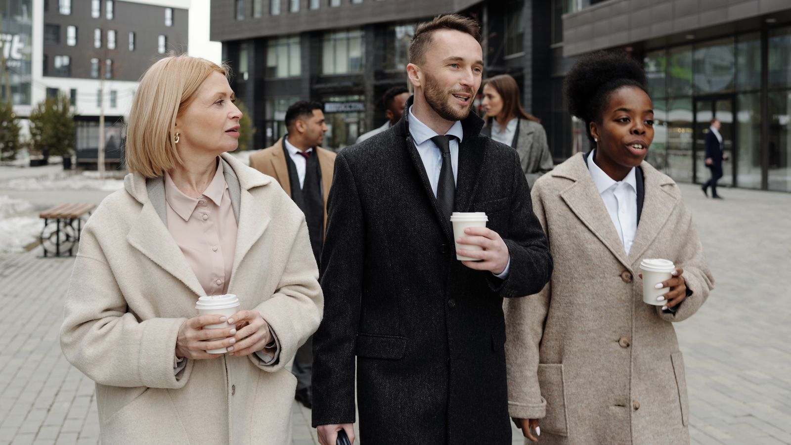 Two coworkers walking outdoors with coffee during a break