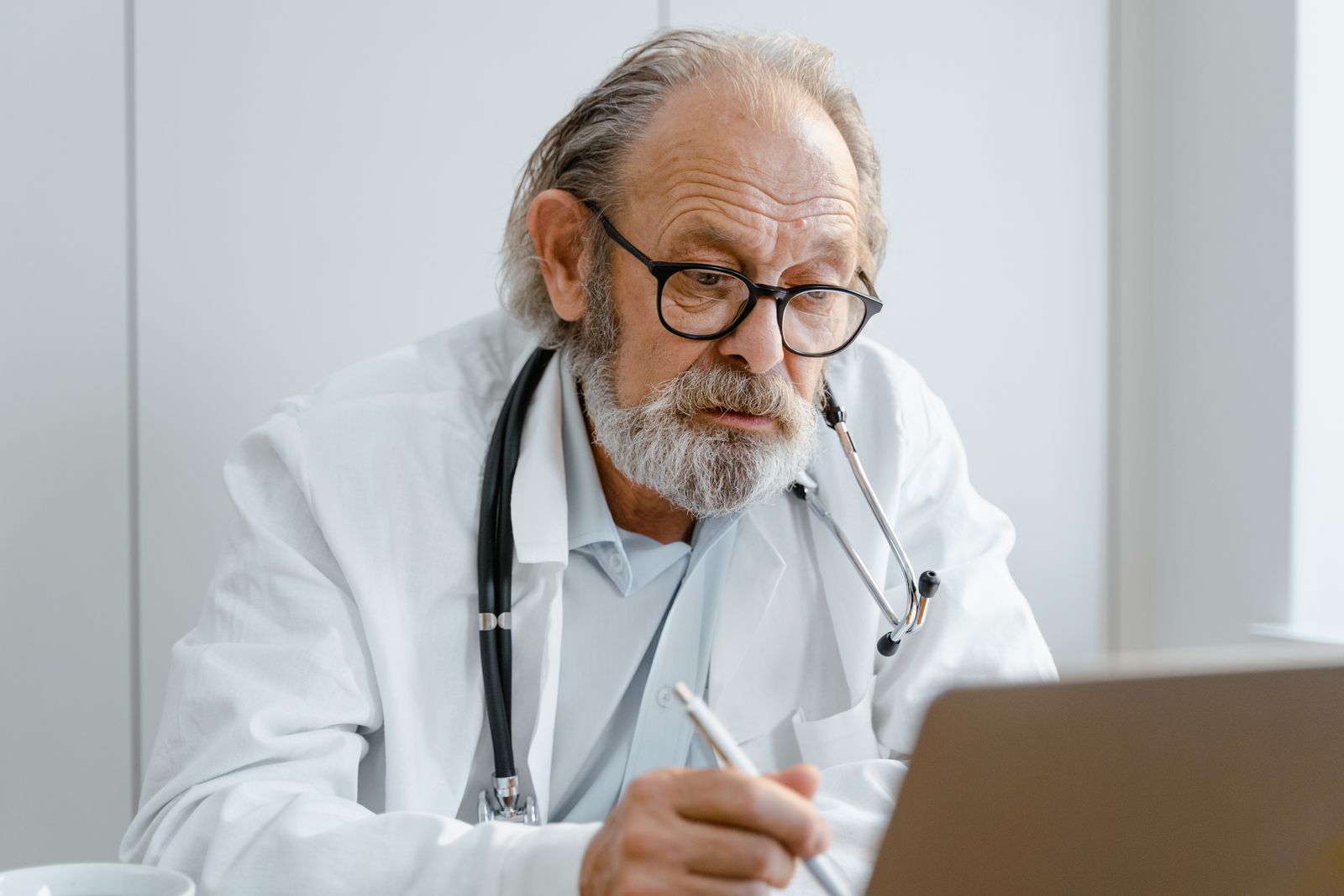 A clinician with glasses working on a laptop in a medical office