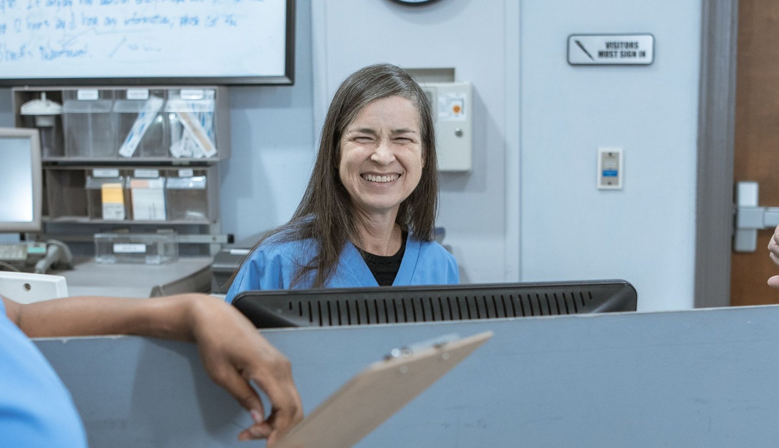 A clinician in blue scrubs smiling at a clinic desk