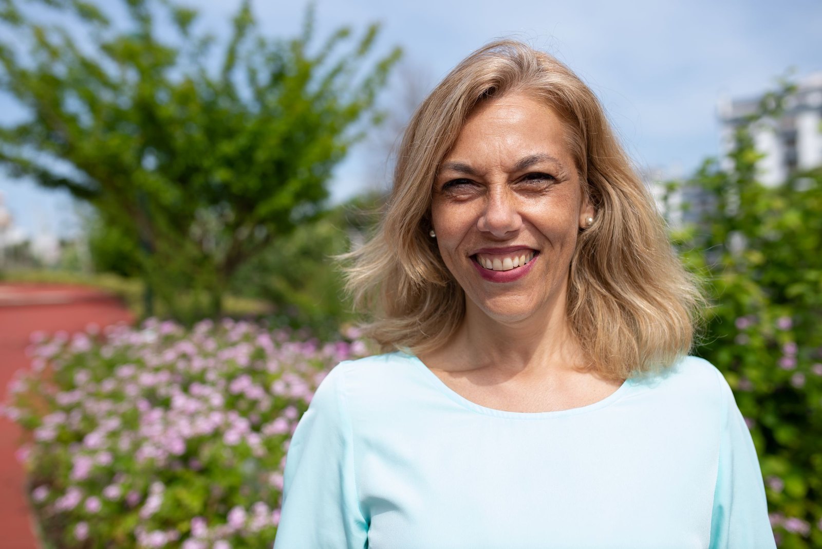 A woman smiling outdoors in a sunny garden