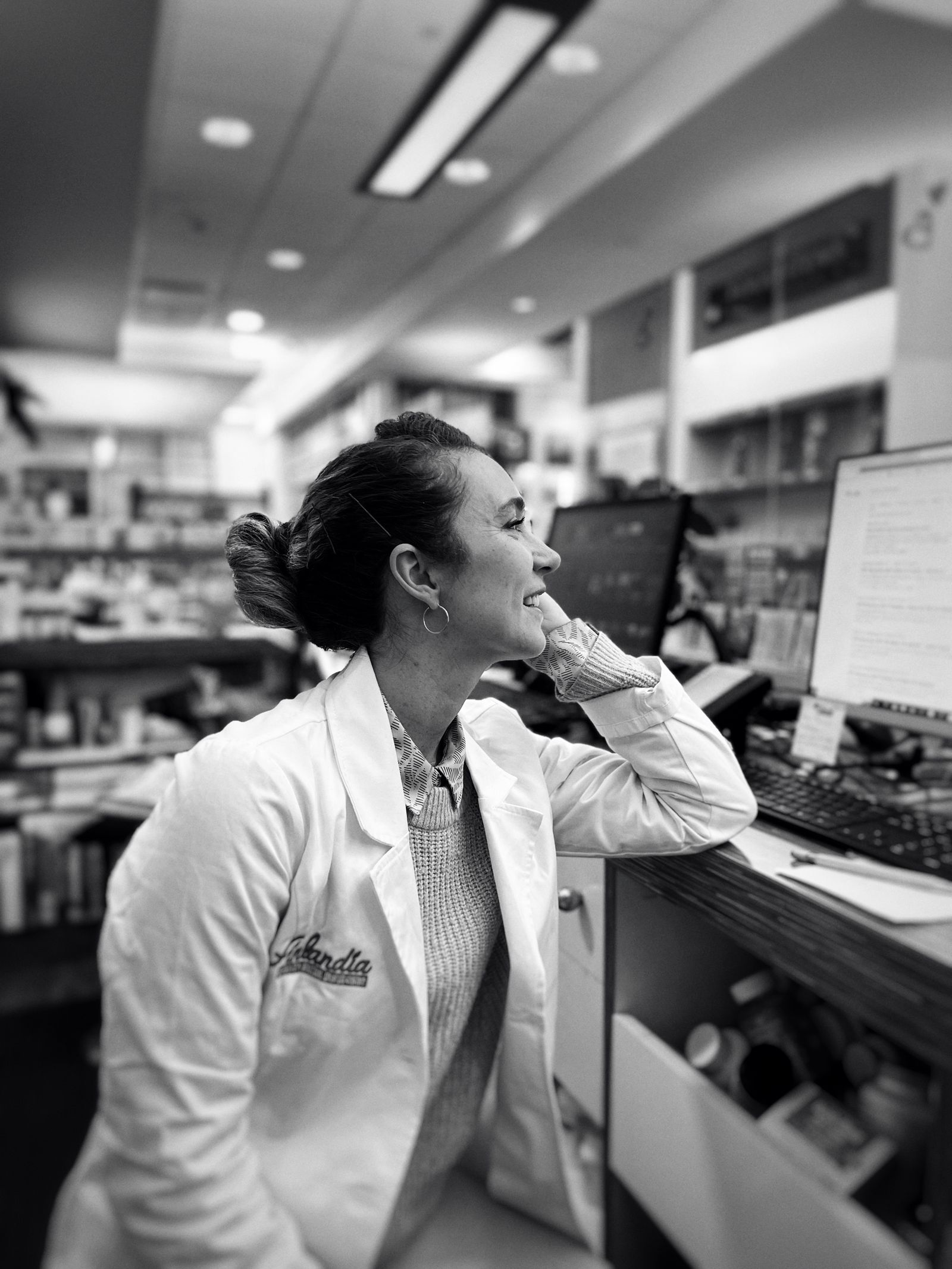 A pharmacist in a white coat at a computer in a pharmacy