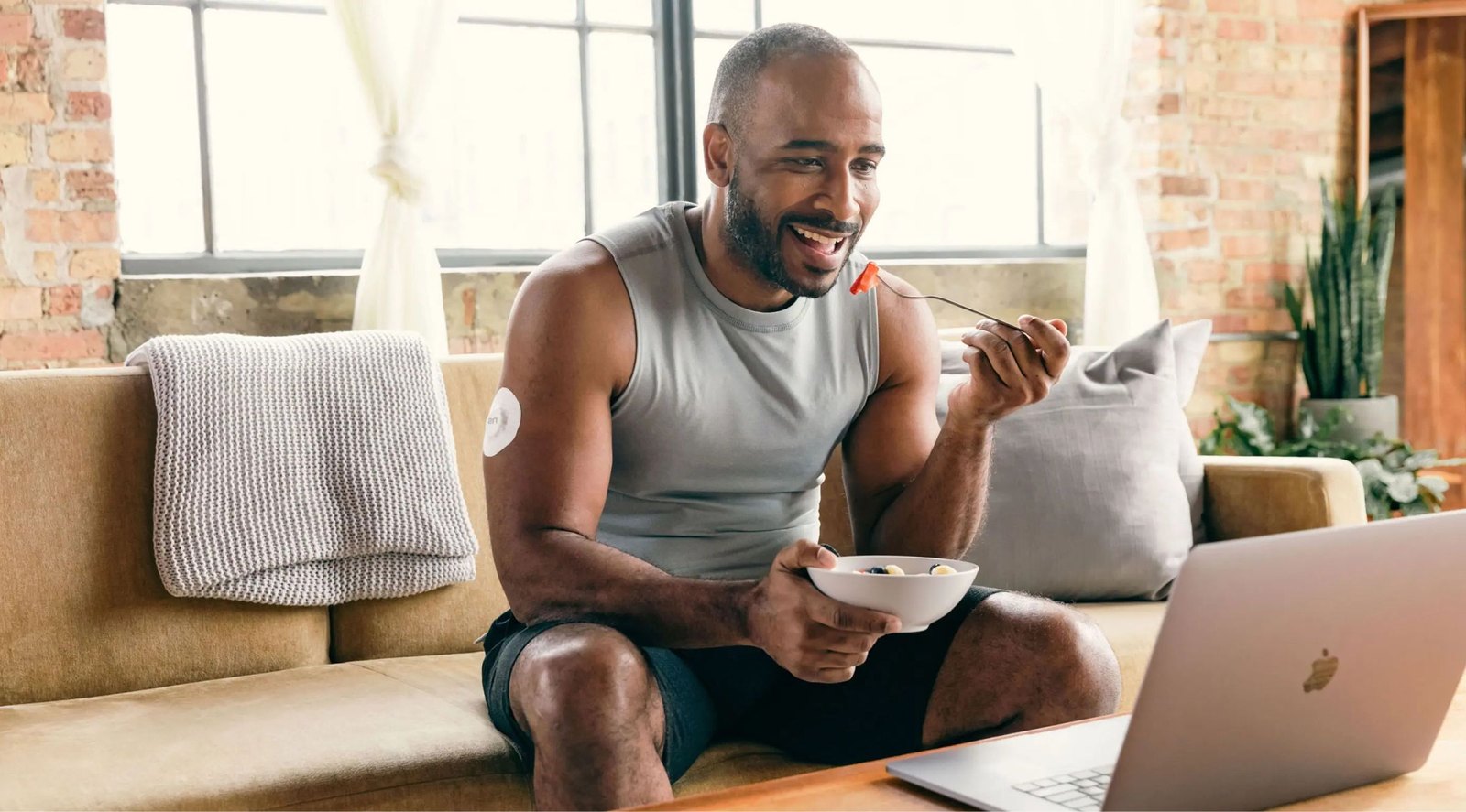 A man at breakfast looking at a laptop, with a glucose sensor on his arm