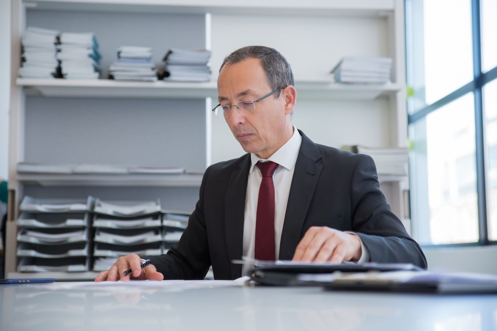 A man in glasses reading papers at a desk