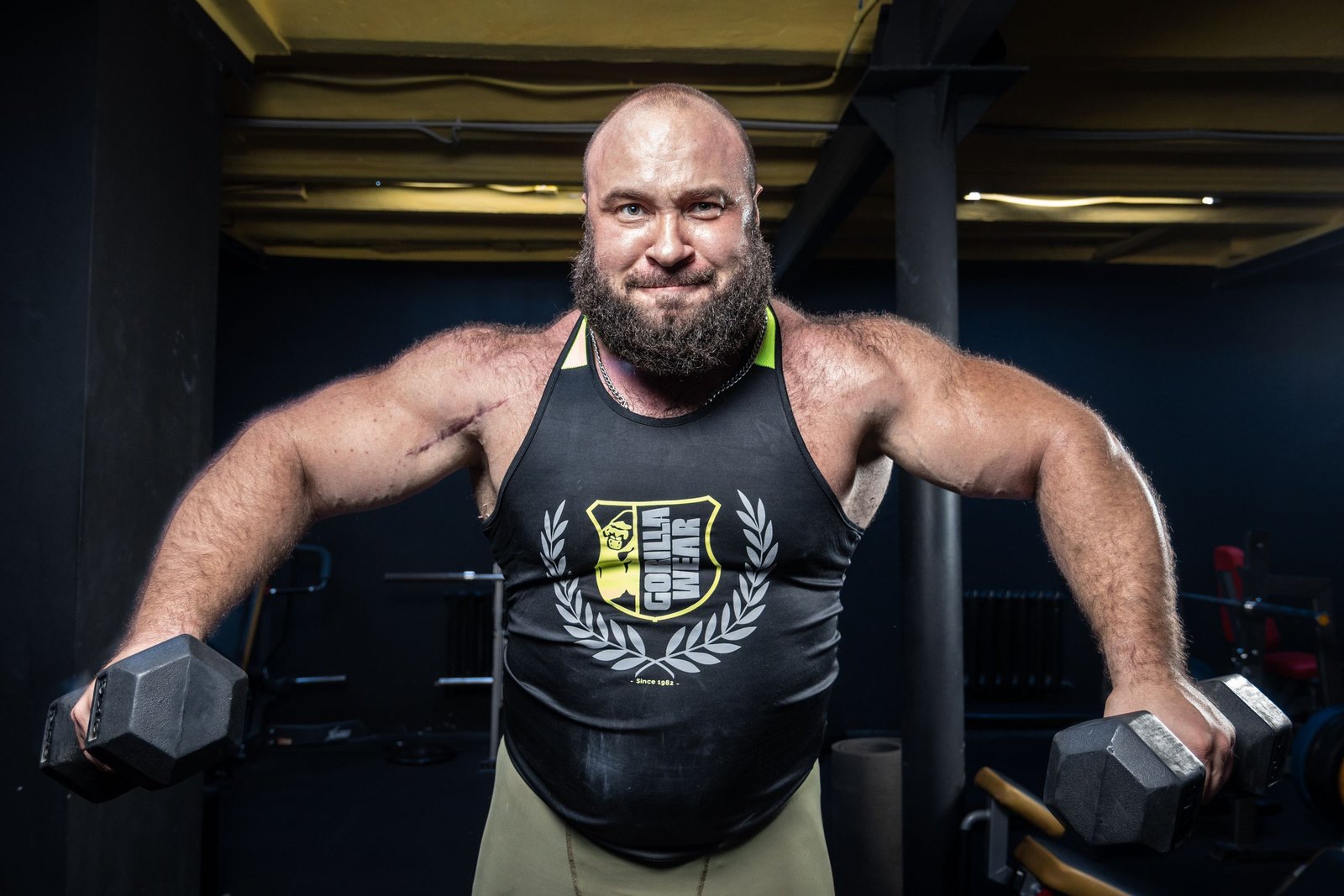 A muscular man in a gym holding a dumbbell in each hand