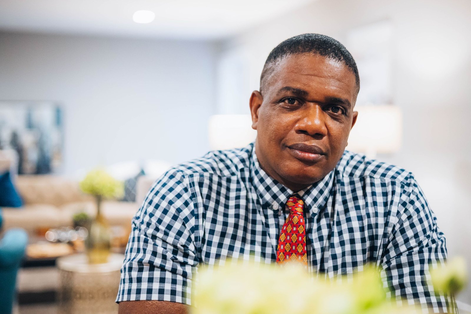 A calm man seated at home, smiling softly at the camera
