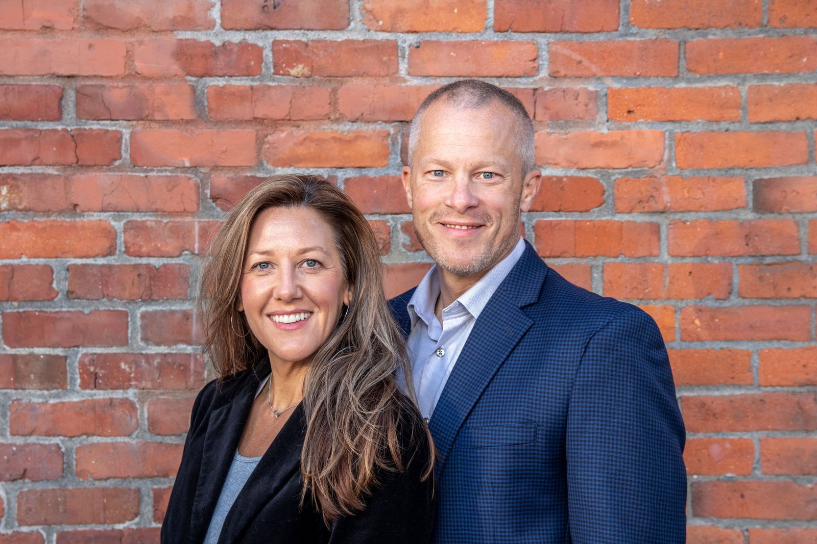 A smiling couple standing together outdoors by a brick wall