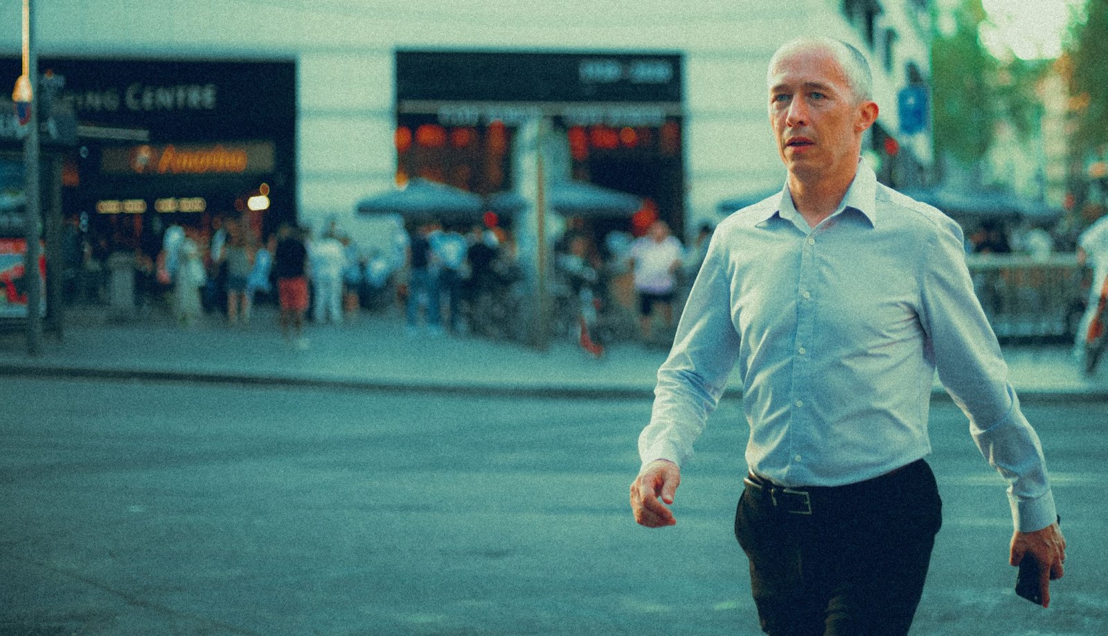 A man in a light blue shirt walking along a busy city sidewalk.