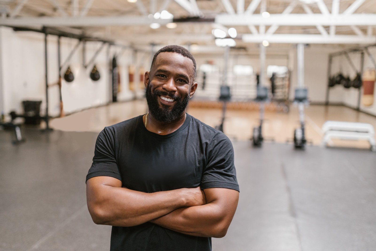 A man standing in a strength gym with his arms crossed, smiling