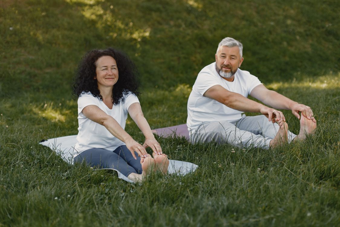 Two adults stretching together outdoors on a lawn